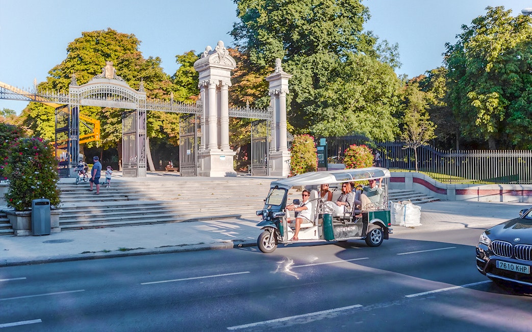Electric tuk-tuk passing Puerta de España gate in Madrid, Spain.