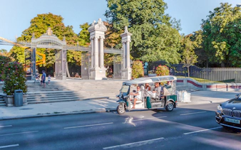 Electric tuk-tuk passing Puerta de España gate in Madrid, Spain.
