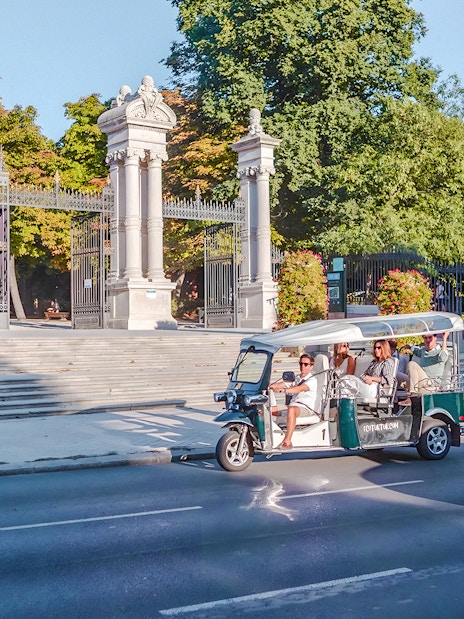 Electric tuk-tuk passing Puerta de España gate in Madrid, Spain.