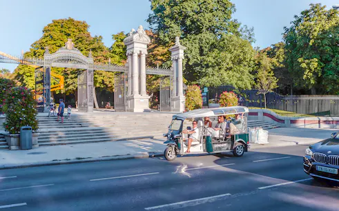 Electric tuk-tuk passing Puerta de España gate in Madrid, Spain.