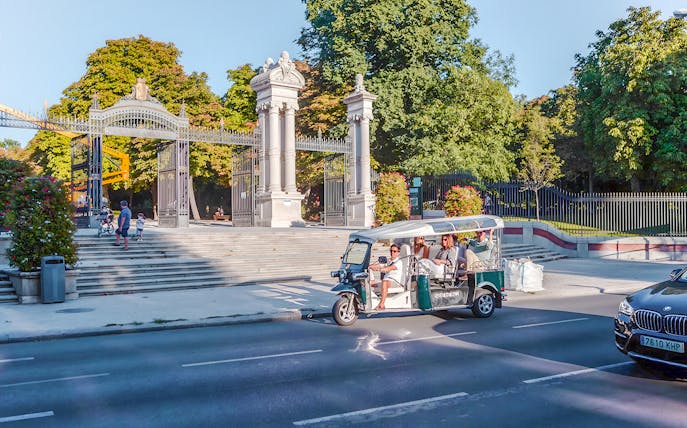Electric tuk-tuk passing Puerta de España gate in Madrid, Spain.