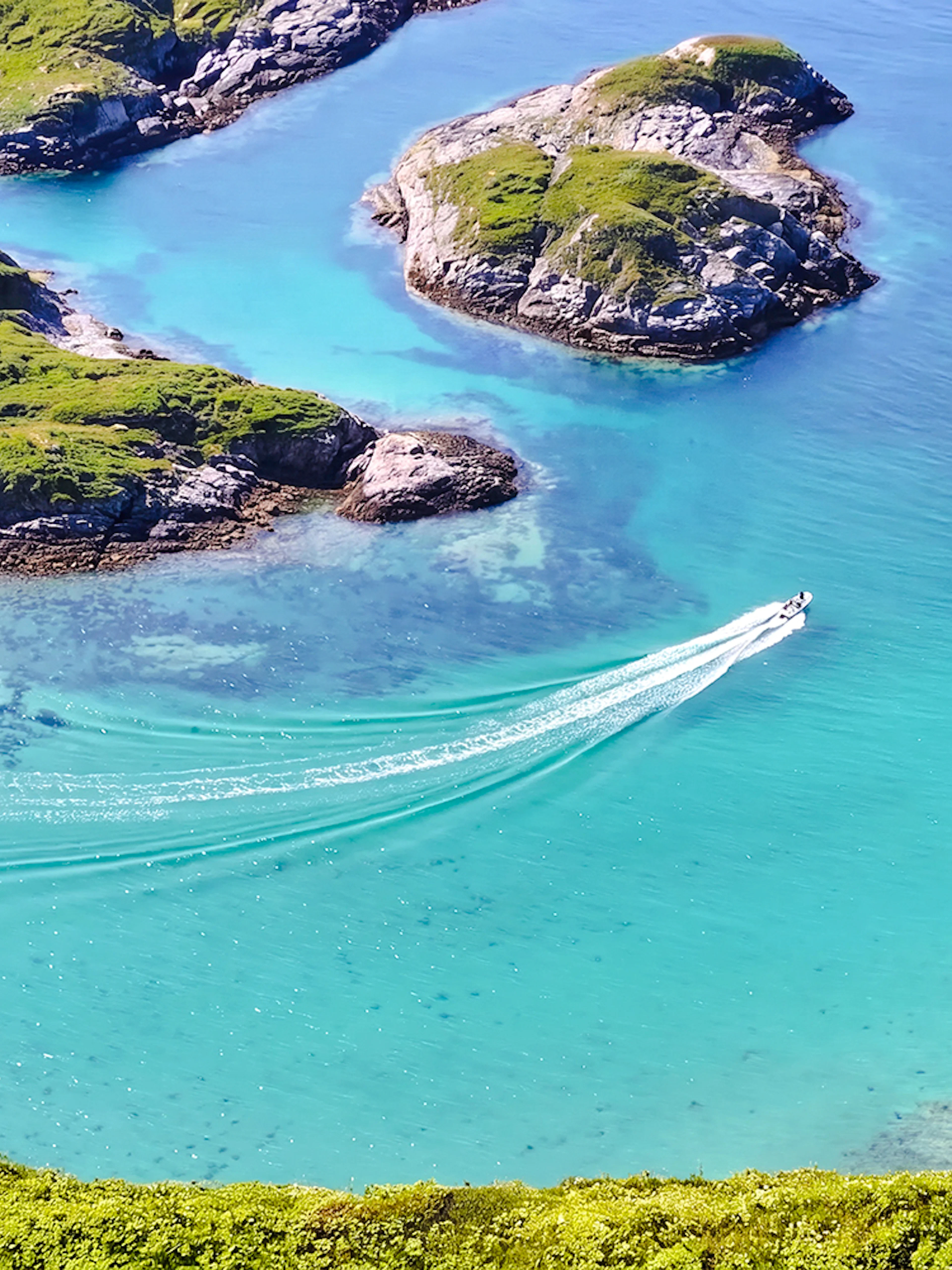Boat cruising through turquoise waters of Sommarøy Fjord, Tromsø, surrounded by green islands.