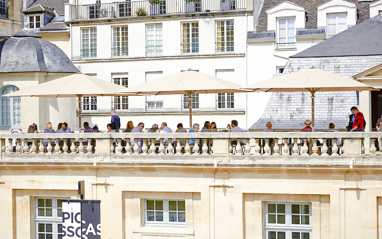 Terrace cafe at Picasso Museum, Paris, with people dining under umbrellas.