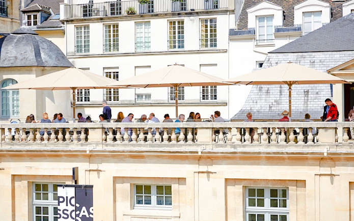 Terrace cafe at Picasso Museum, Paris, with people dining under umbrellas.