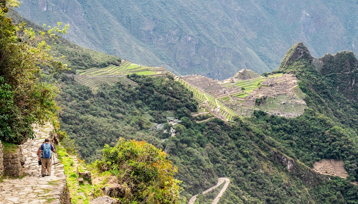 Hiker approaching Machu Picchu view from Sun Gate on Inca Trail, Peru.