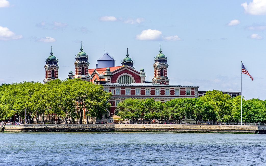Ellis Island with historic building viewed from East River cruise near Statue of Liberty.