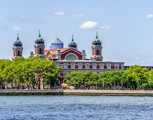 Ellis Island with historic building viewed from East River cruise near Statue of Liberty.