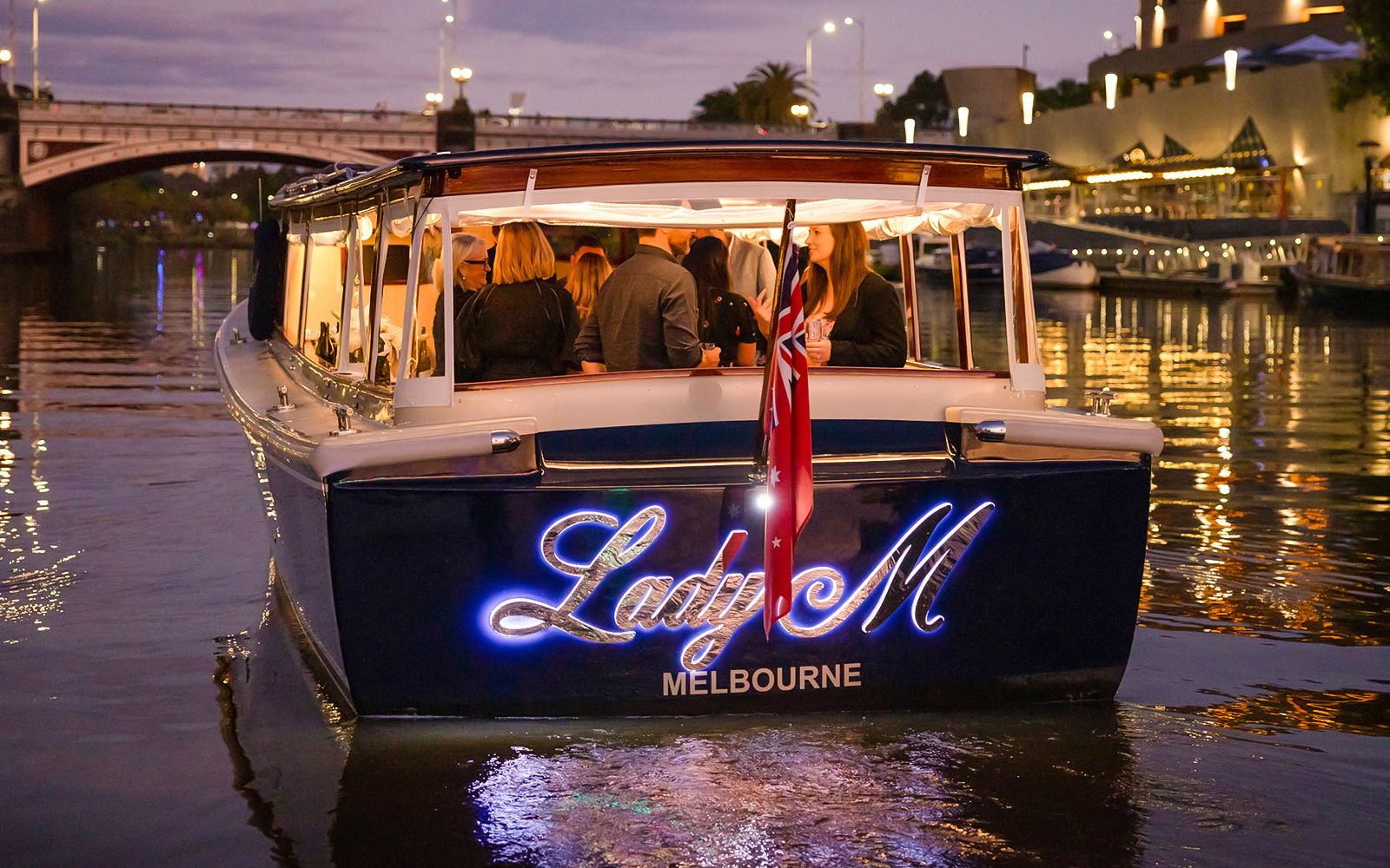 Luxury cruise boat on Yarra River at sunset with Melbourne city lights.