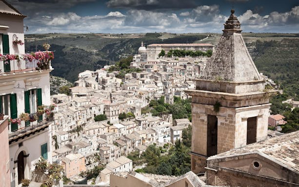 Ragusa cityscape with historic buildings and distant hills, view from a minivan tour.