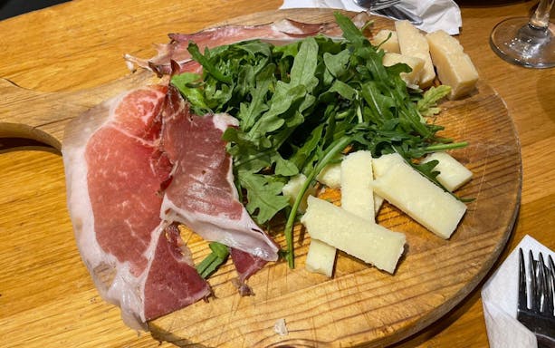 Cured meats, arugula, and cheese on a wooden platter during Trastevere food tour.