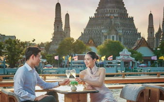 Couple enjoying a drink on Okura Cruise with Wat Arun in the background, Bangkok.