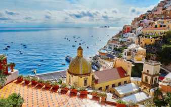 Positano village on Amalfi Coast with colorful buildings and dome overlooking the Mediterranean Sea.