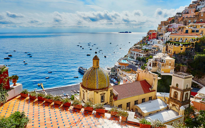 Positano village on Amalfi Coast with colorful buildings and dome overlooking the Mediterranean Sea.