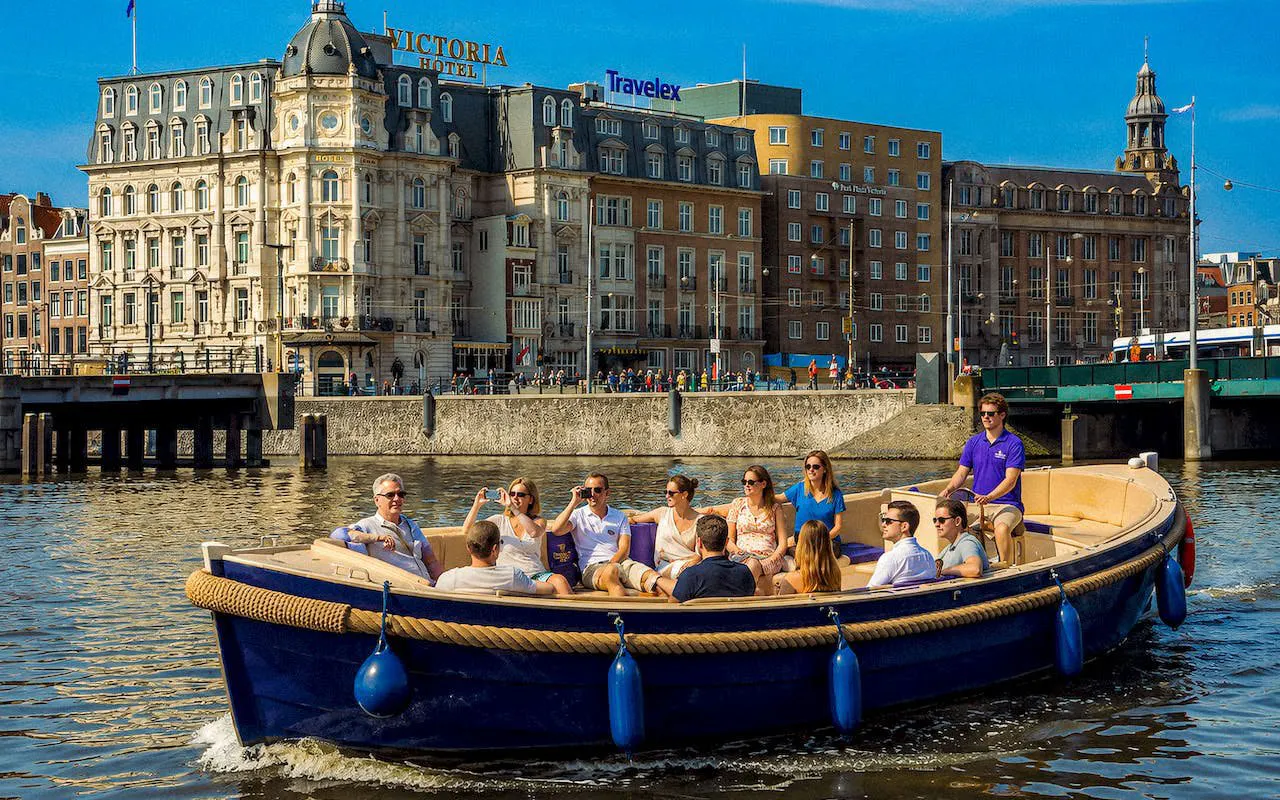 Open boat with tourists cruising Amsterdam canal near historic buildings.