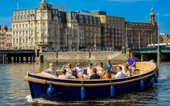 Open boat with tourists cruising Amsterdam canal near historic buildings.