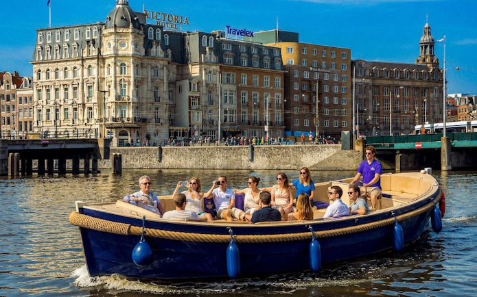 Open boat with tourists cruising Amsterdam canal near historic buildings.
