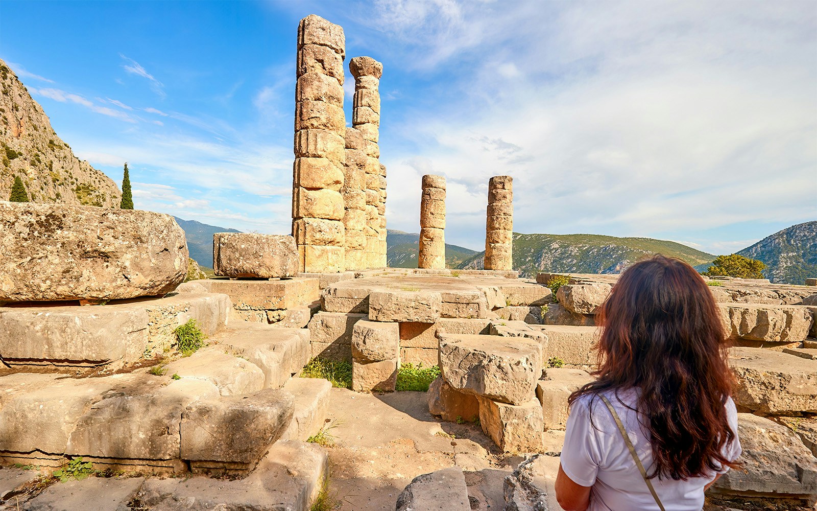 Temple of Apollo ruins at Delphi archaeological site with visitor in foreground.
