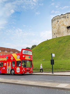 Red double-decker bus for city sightseeing in York near Clifford's Tower.