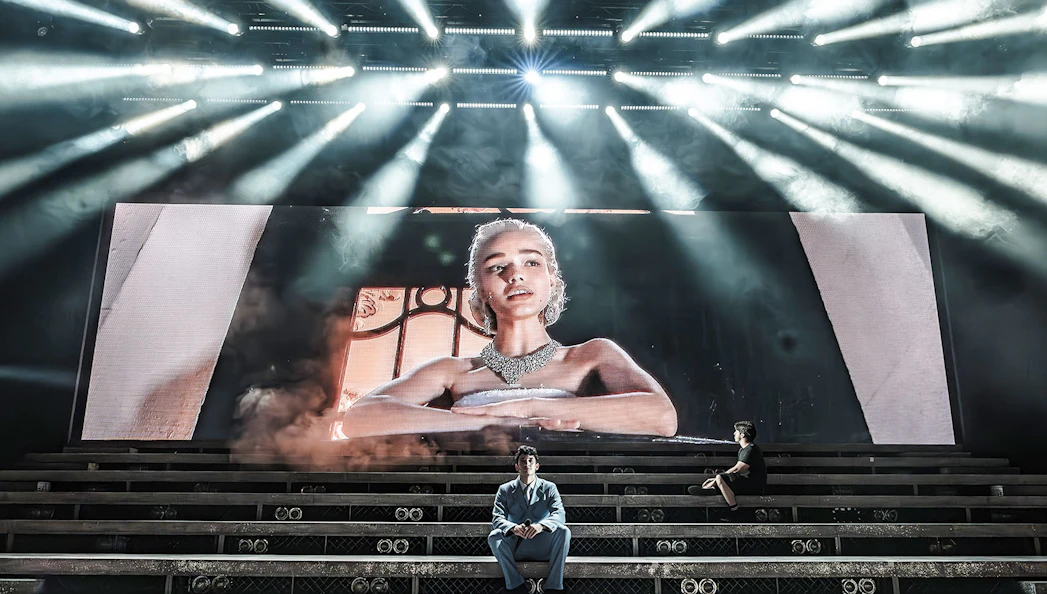 Stage scene from Evita Musical with large screen portrait and performers on steps.