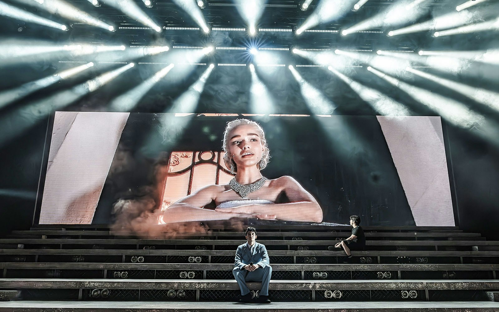 Stage scene from Evita Musical with large screen portrait and performers on steps.