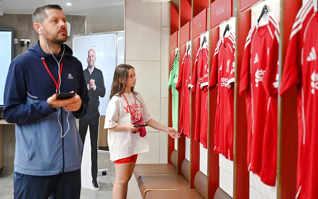 Visitors exploring the players' dressing room at Anfield Arena with team jerseys displayed.