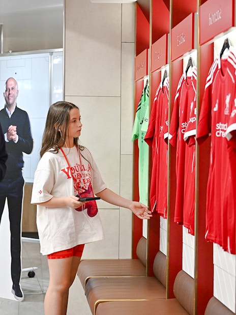Visitors exploring the players' dressing room at Anfield Arena with team jerseys displayed.