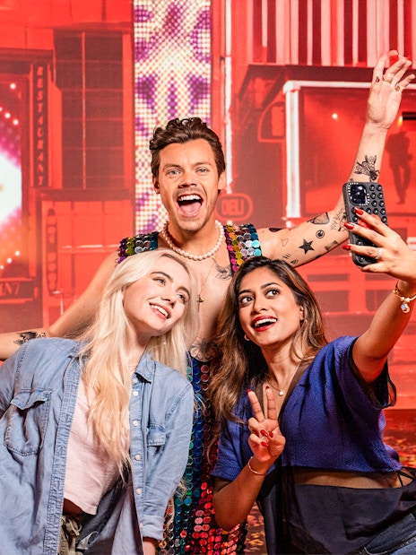 Two women taking a selfie with Harry Styles's wax figure at Madame Tussauds, New York.