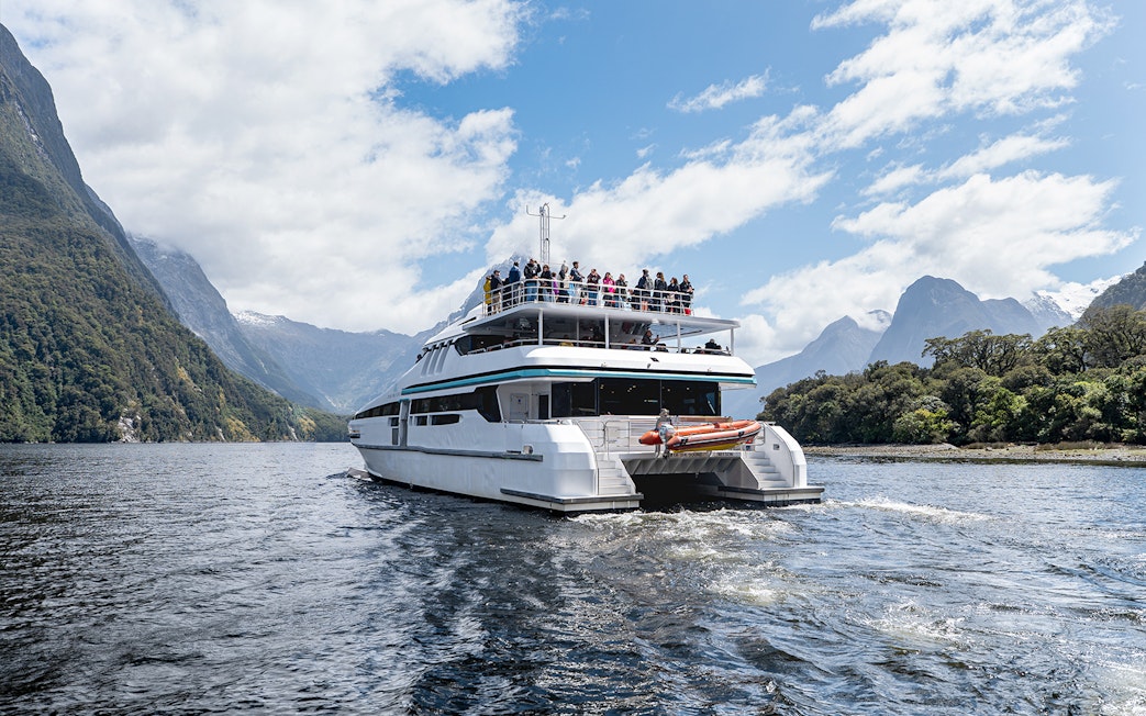 Cruise boat on Milford Sound with passengers viewing scenic mountains.