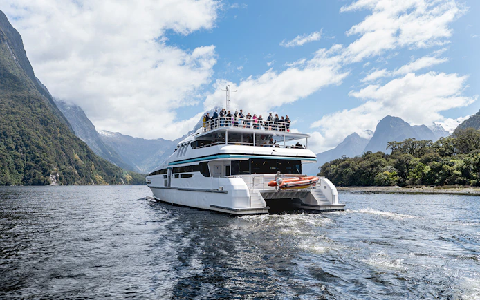 Cruise boat on Milford Sound with passengers viewing scenic mountains.