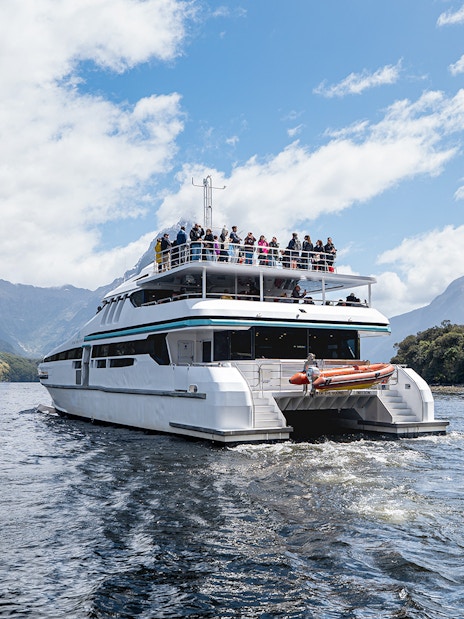 Cruise boat on Milford Sound with passengers viewing scenic mountains.