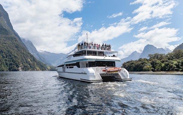 Cruise boat on Milford Sound with passengers viewing scenic mountains.