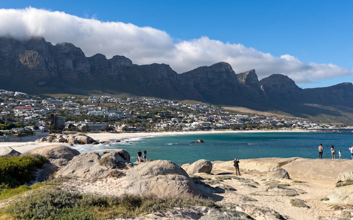Cape Town coastline with Twelve Apostles mountain range and tourists exploring the rocky shore.