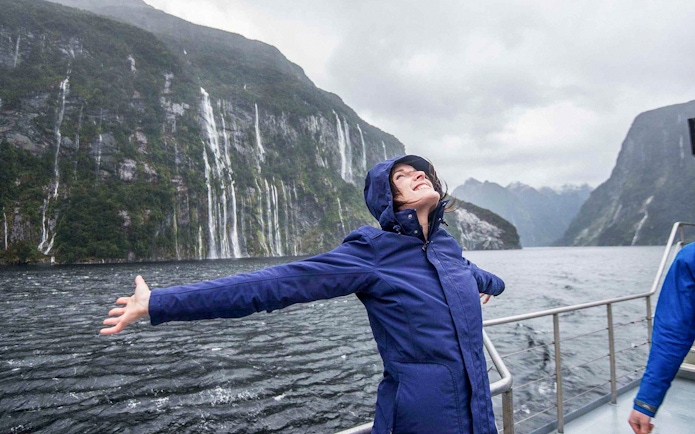 Person enjoying the view of waterfalls and mountains on a Doubtful Sound cruise from Te Anau.