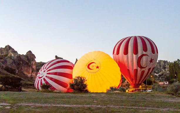 Hot air balloons inflating at sunrise near Cappadocia's fairy chimneys.