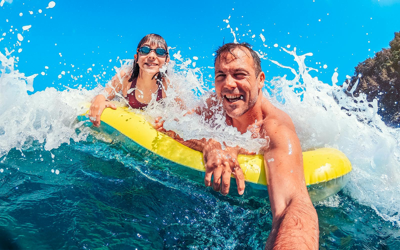 Father and daughter on a yellow float in ocean waves, enjoying a beach day.