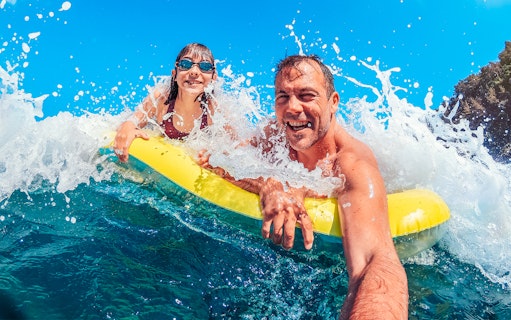 Father and daughter on a yellow float in ocean waves, enjoying a beach day.