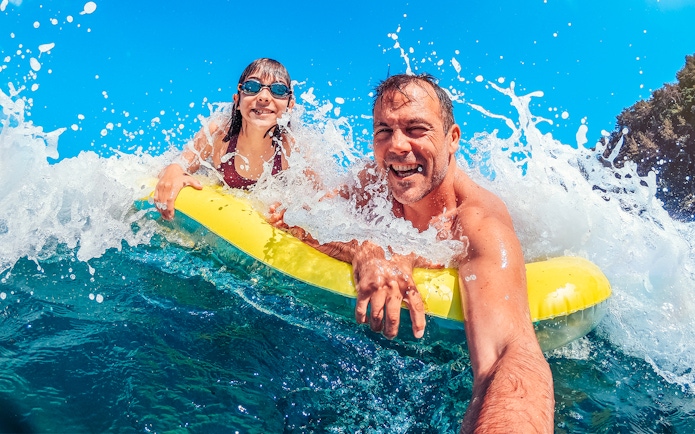 Father and daughter on a yellow float in ocean waves, enjoying a beach day.