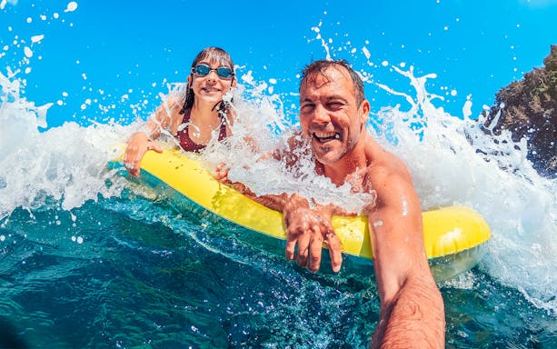 Father and daughter on a yellow float in ocean waves, enjoying a beach day.
