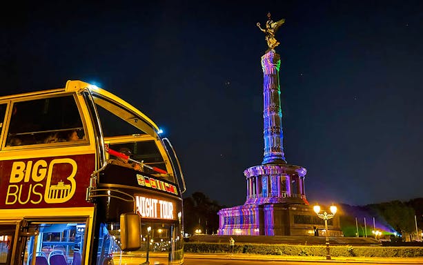 Open-top bus near Berlin's Victory Column illuminated during the Berlin Lights Festival.