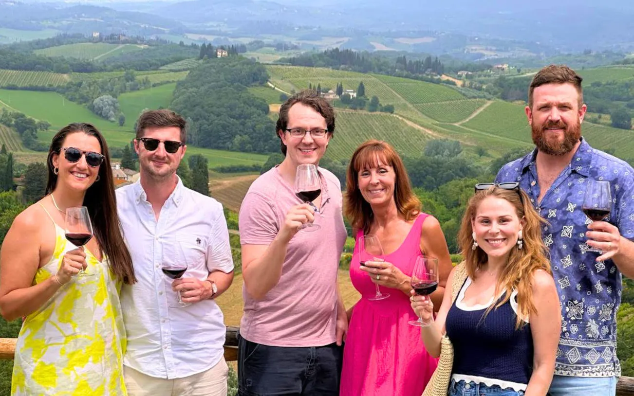 Tourists enjoying wine with a view of Tuscany vineyards during a private tour from Florence.