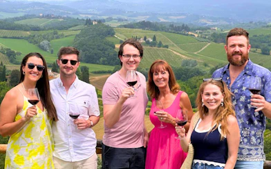Tourists enjoying wine with a view of Tuscany vineyards during a private tour from Florence.