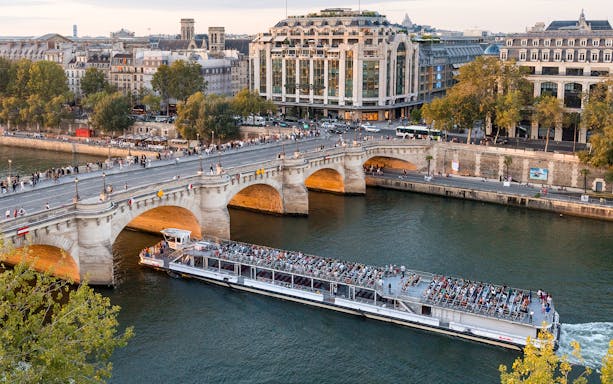 Seine River cruise boat passing under Pont Neuf in Paris with passengers enjoying the view.