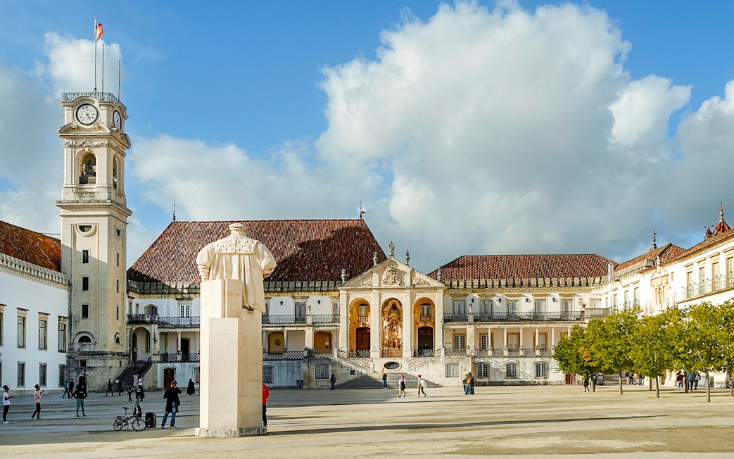 University of Coimbra courtyard with clock tower and statue, part of Fátima & Coimbra tour from Porto.