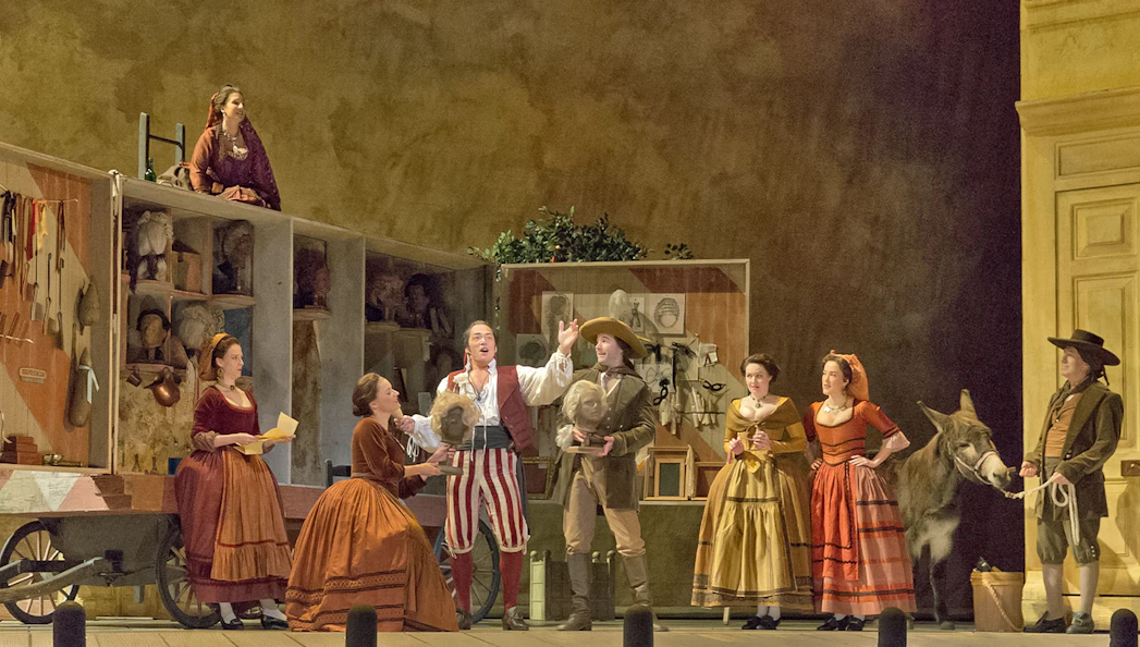 Opera performers on stage during Il Barbiere Di Siviglia with costumes and props.