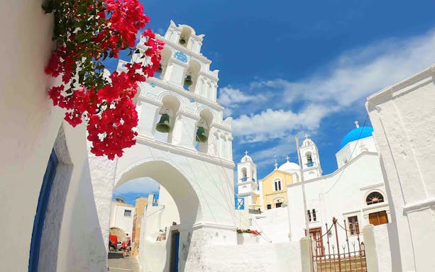 White bell tower and red flowers in Santorini, Greece, on a sunny day.