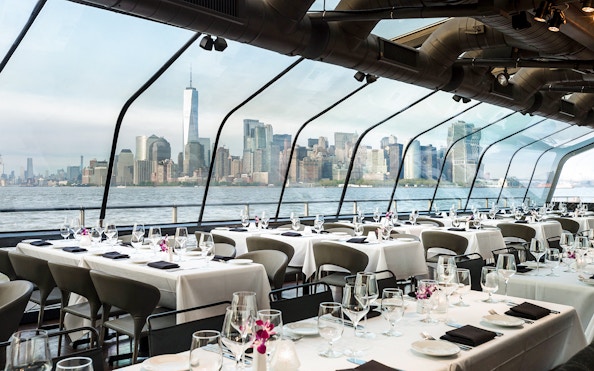Dining tables set on a cruise ship with a view of New York City skyline.
