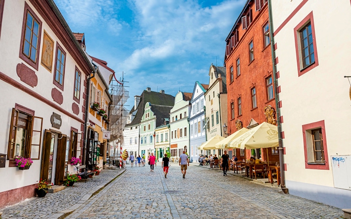 Tourists walking along a cobblestone street in Cesky Krumlov, surrounded by colorful historic buildings.