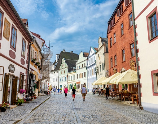 Tourists walking along a cobblestone street in Cesky Krumlov, surrounded by colorful historic buildings.