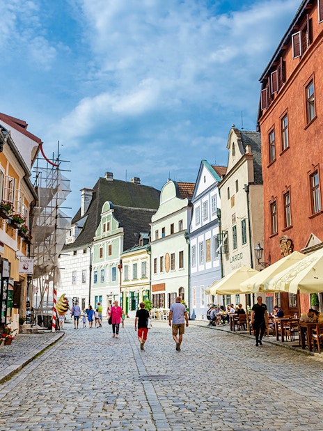 Tourists walking along a cobblestone street in Cesky Krumlov, surrounded by colorful historic buildings.
