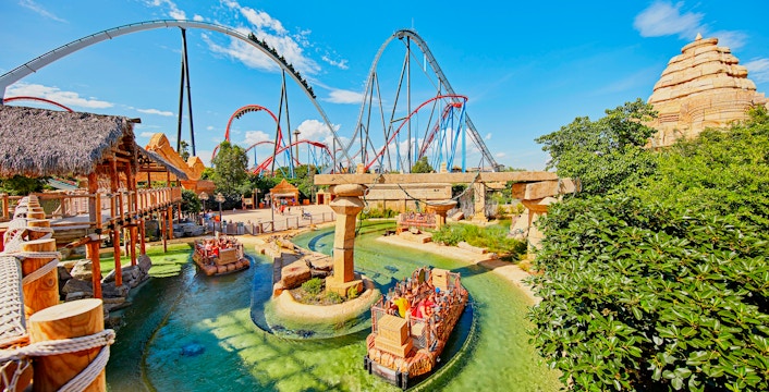 Visitors on a water ride at Port Aventura World with roller coasters in the background.